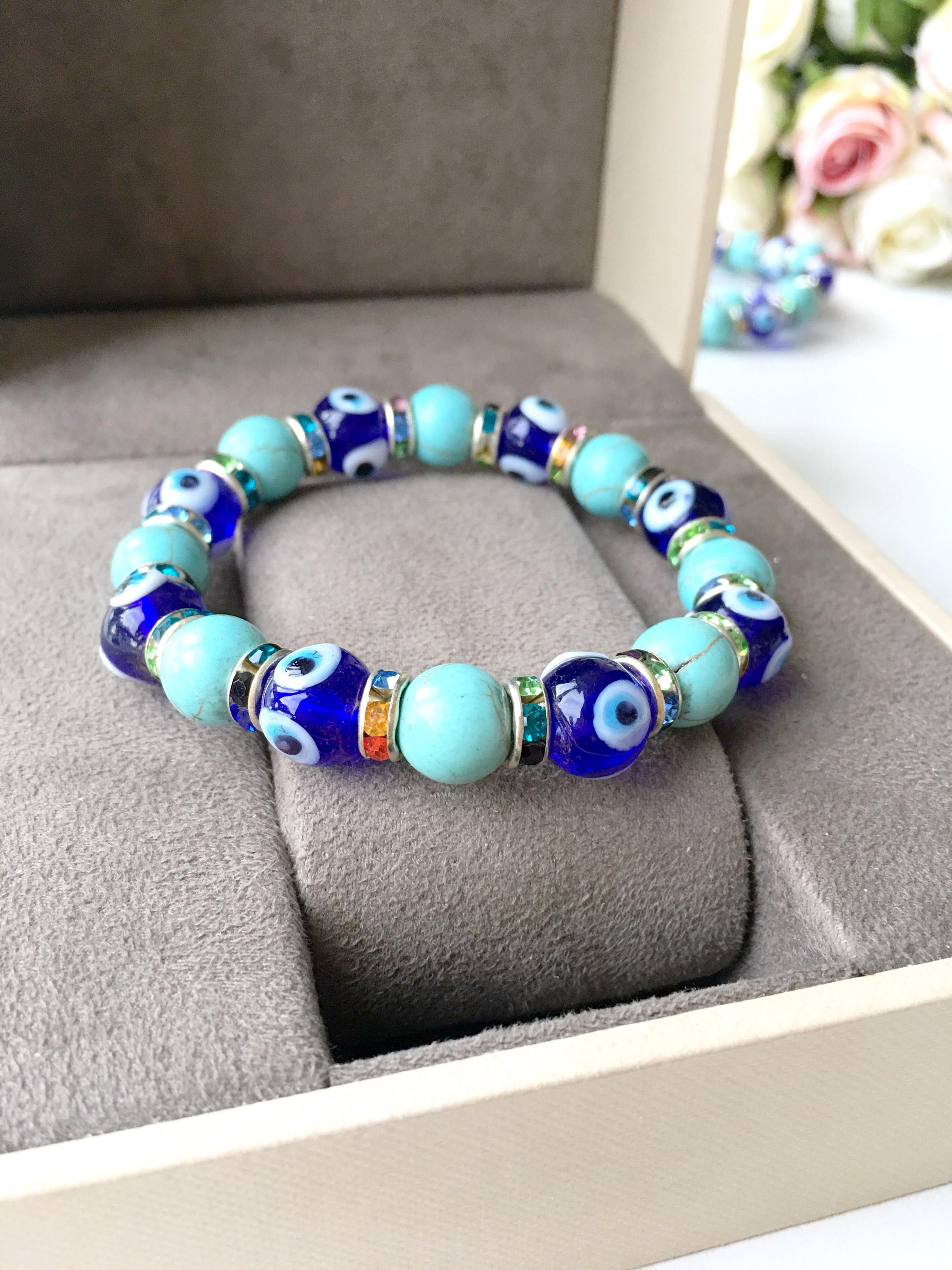 A beautiful blue evil eye bracelet made of glass beads, featuring turquoise accents and a protective charm, elegantly displayed on a soft surface.