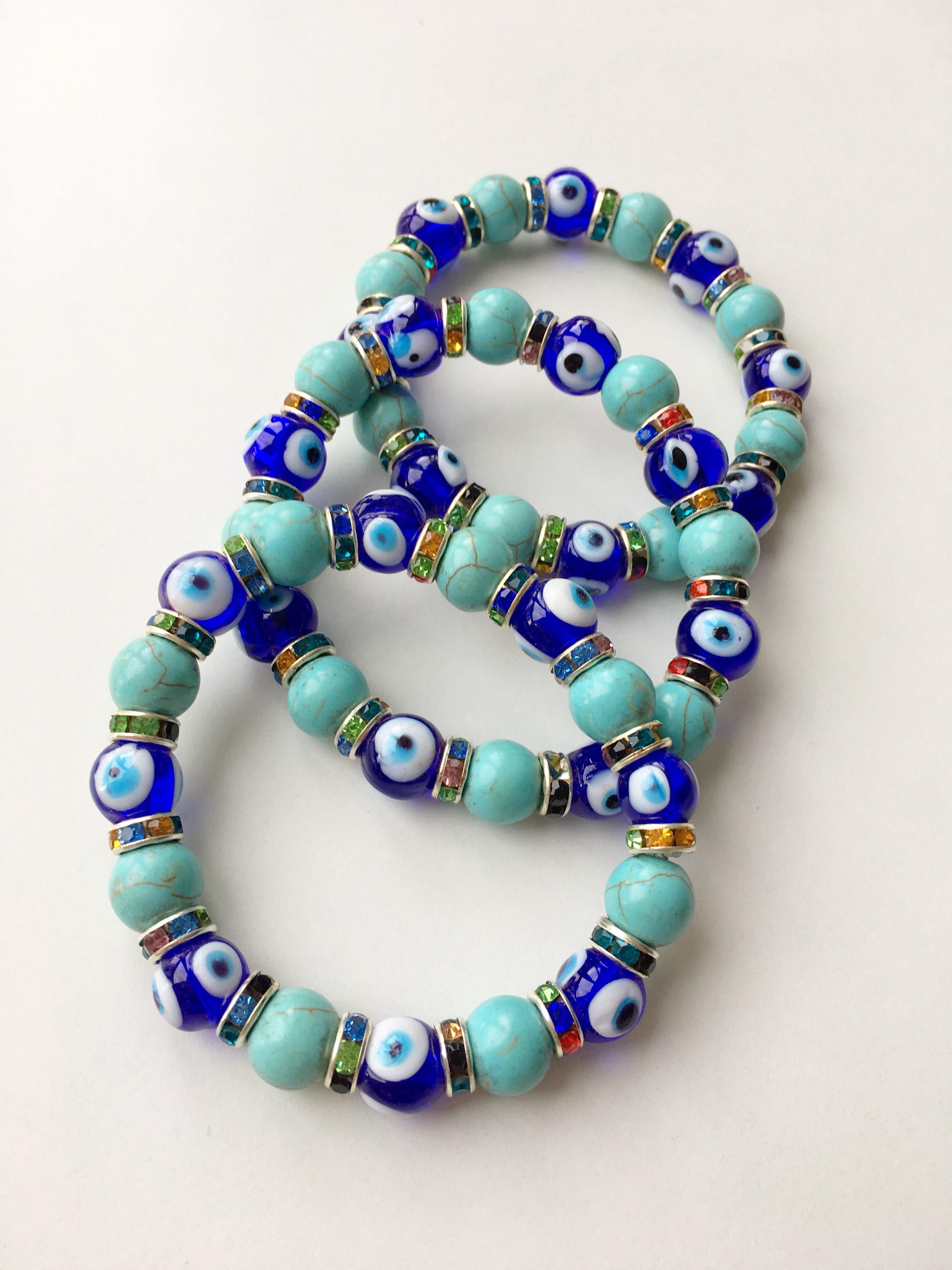 A beautiful blue evil eye bracelet made of glass beads, featuring turquoise accents and a protective charm, elegantly displayed on a soft surface.