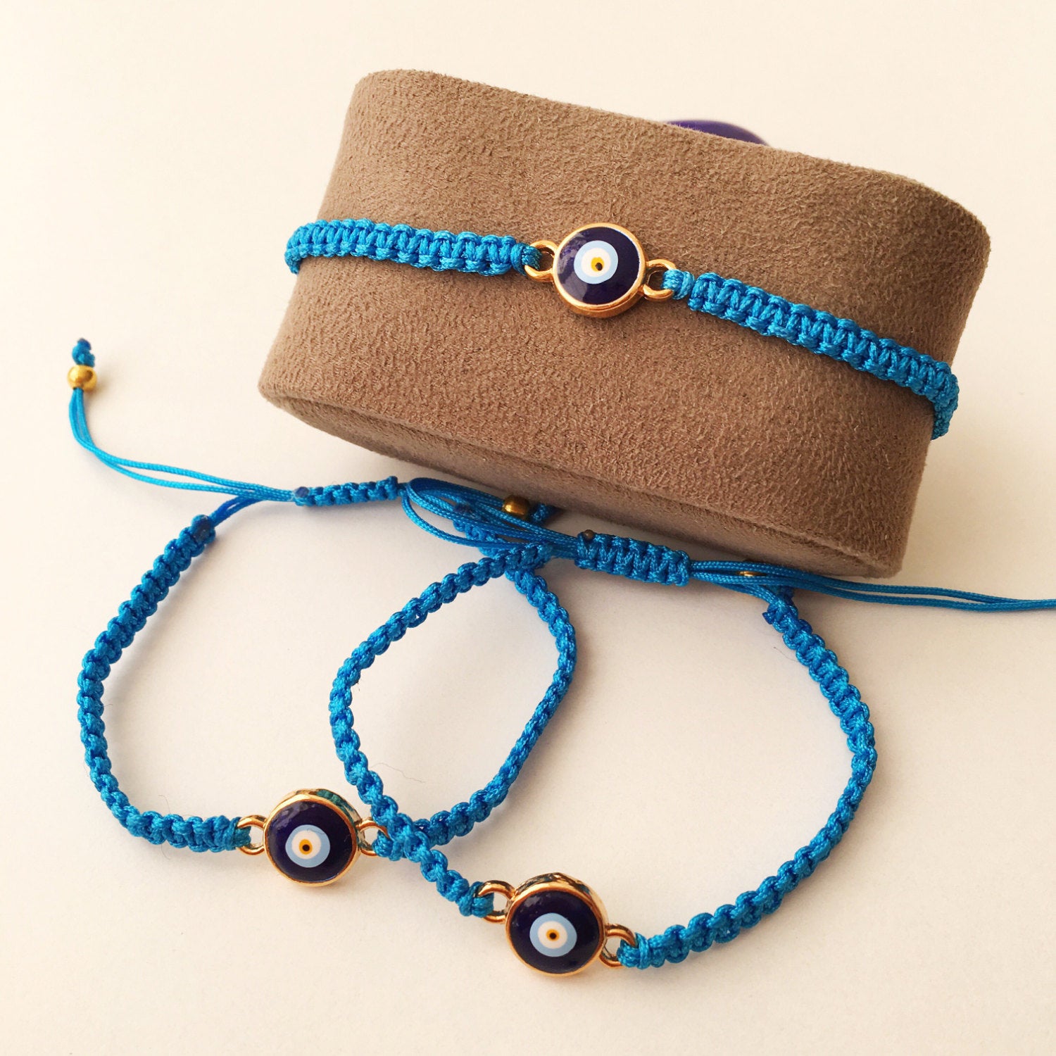 A handmade Blue Evil Eye Bracelet featuring a turquoise string and a black macramé design, showcasing a blue evil eye charm in the center.