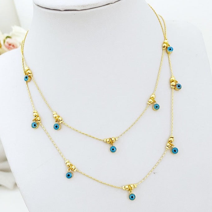 A delicate blue evil eye necklace featuring a blue glass bead on a gold plated brass chain, showcasing its dainty design and adjustable length.