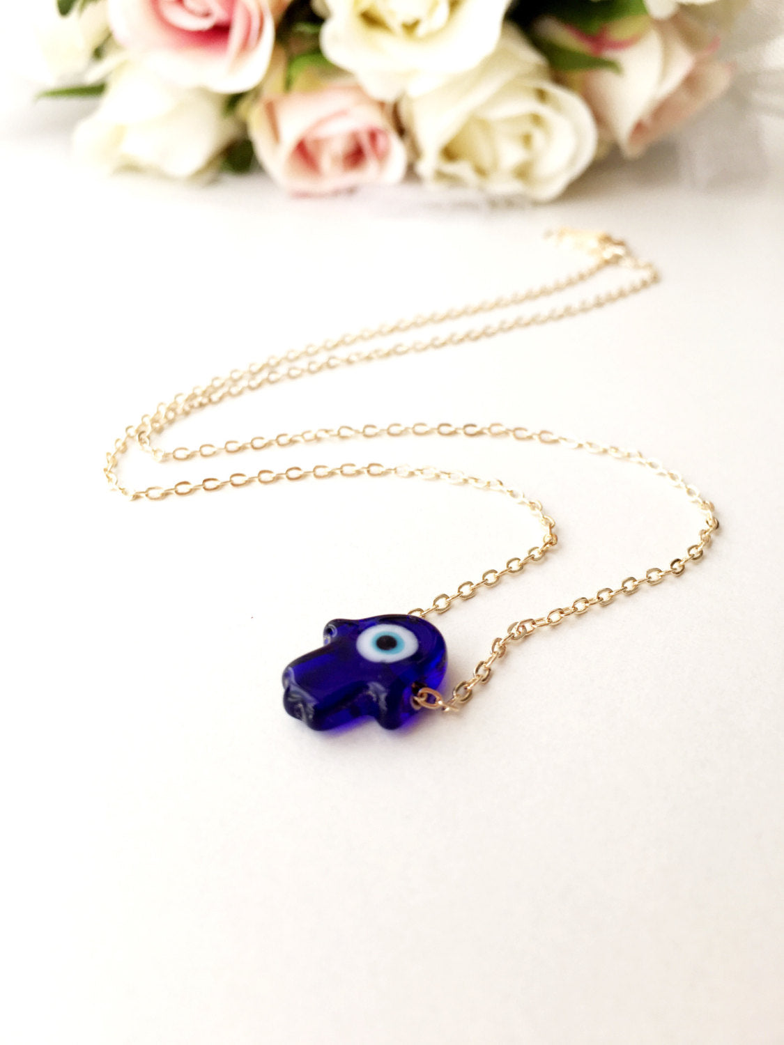 A stunning blue evil eye necklace featuring a glass hamsa hand on a gold plated chain, symbolizing protection and good fortune.