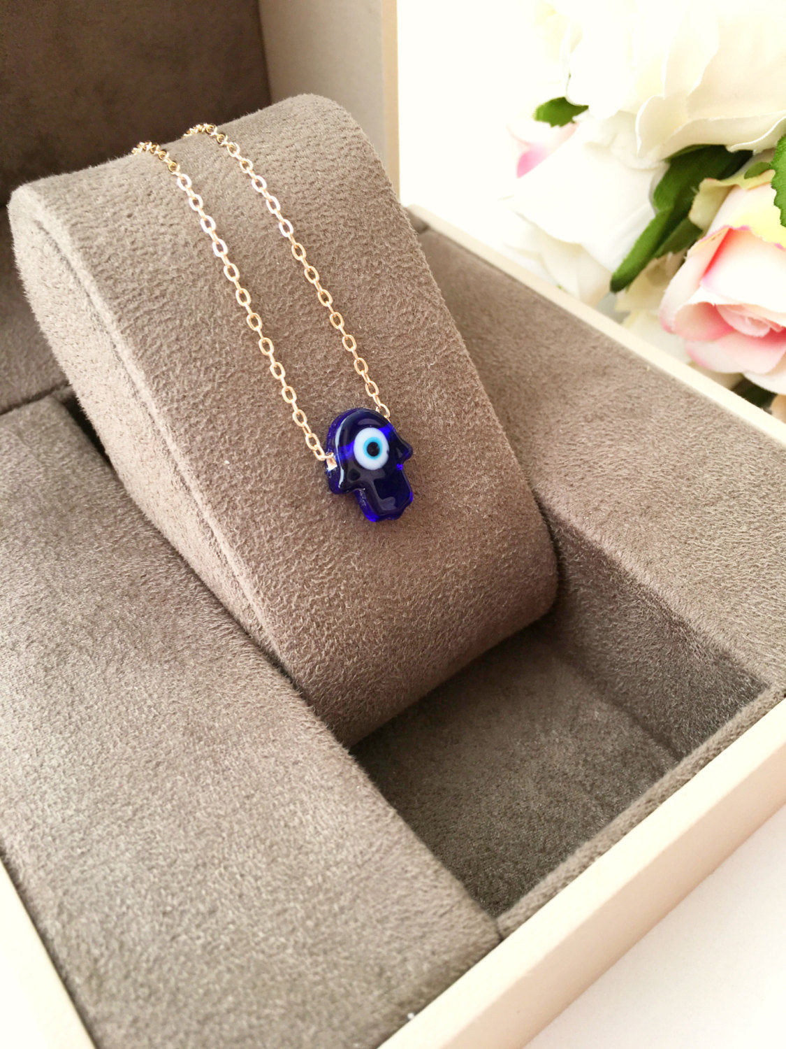 A stunning blue evil eye necklace featuring a glass hamsa hand on a gold plated chain, symbolizing protection and good fortune.