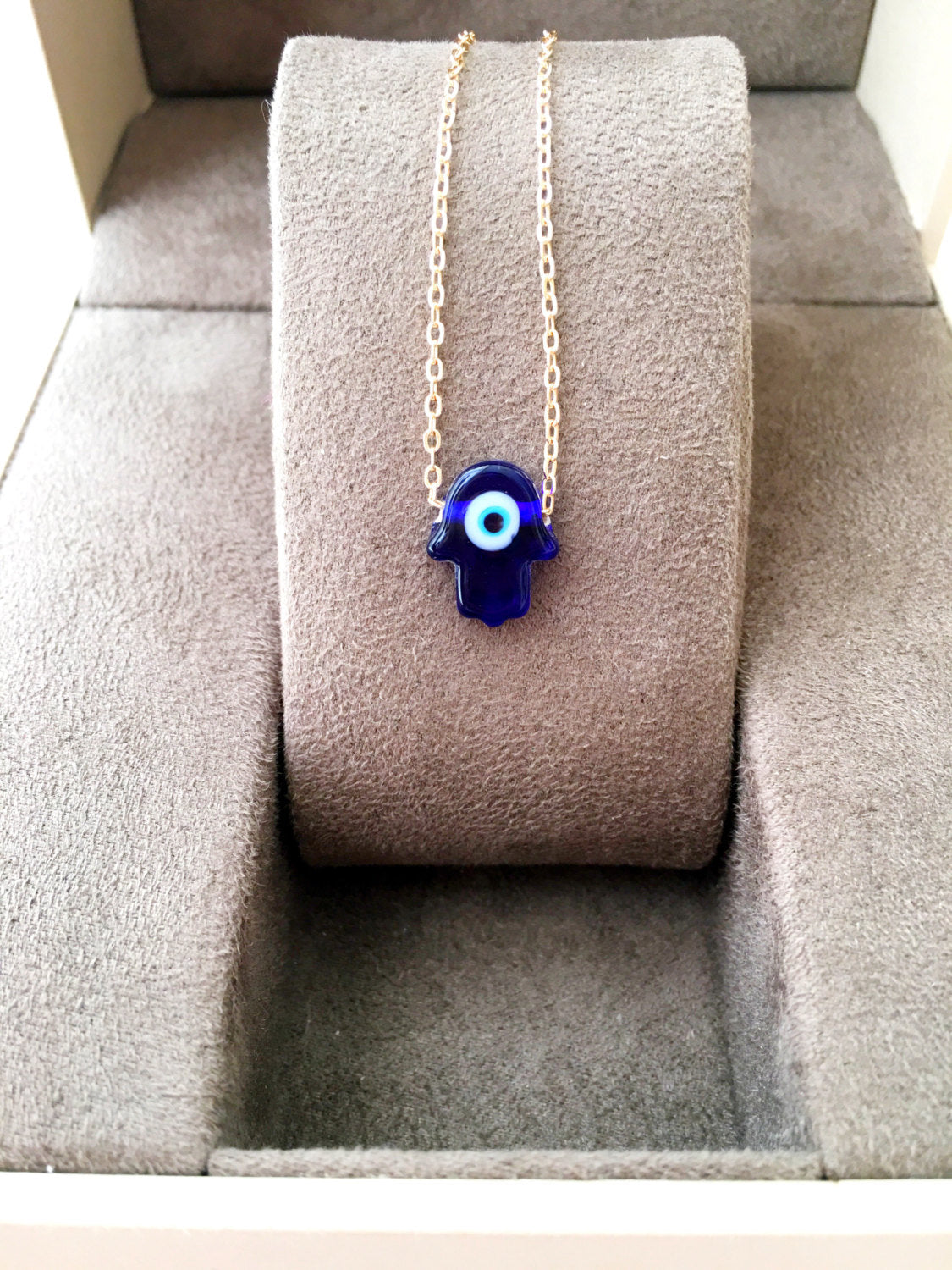 A stunning blue evil eye necklace featuring a glass hamsa hand on a gold plated chain, symbolizing protection and good fortune.