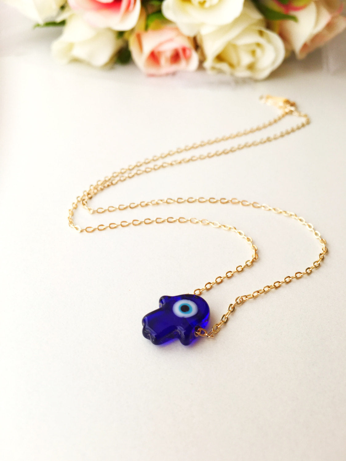 A stunning blue evil eye necklace featuring a glass hamsa hand on a gold plated chain, symbolizing protection and good fortune.