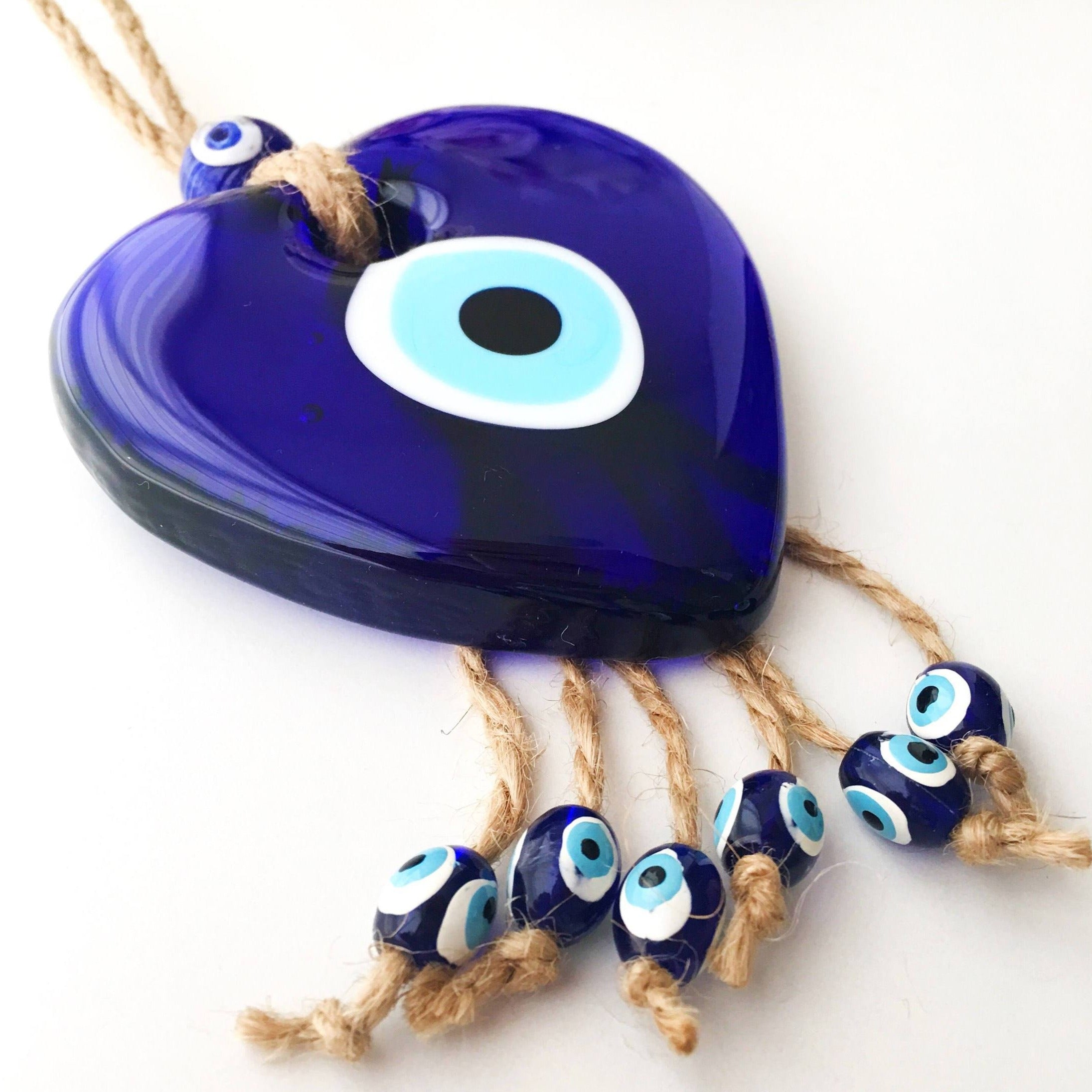 A beautiful Blue Glass Evil Eye Heart Wall Hanging featuring a large heart-shaped glass bead and tiny evil eye beads, intricately designed with macrame.