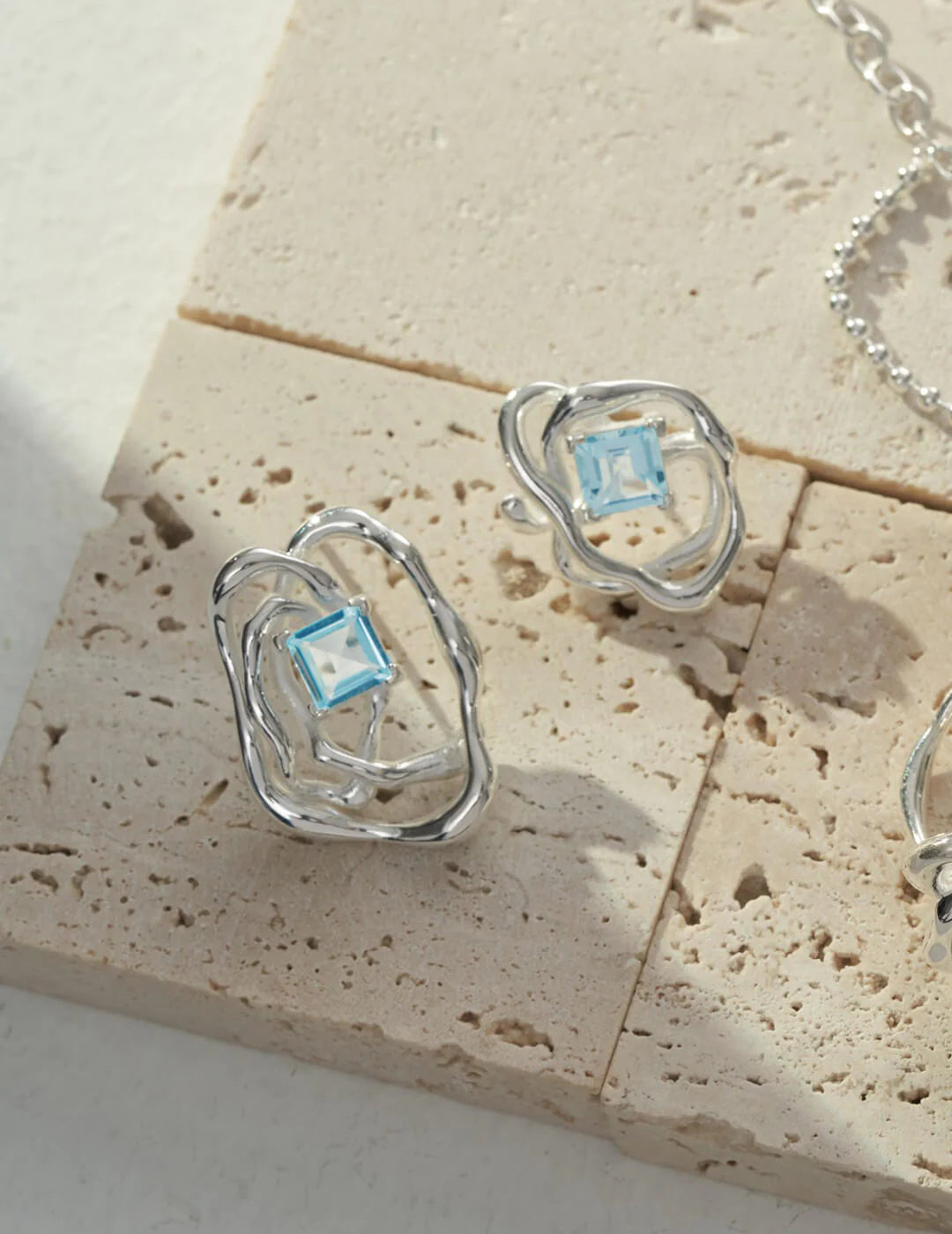 A pair of handcrafted blue topaz statement earrings featuring sterling silver settings, showcasing unique gemstones in varying sizes.