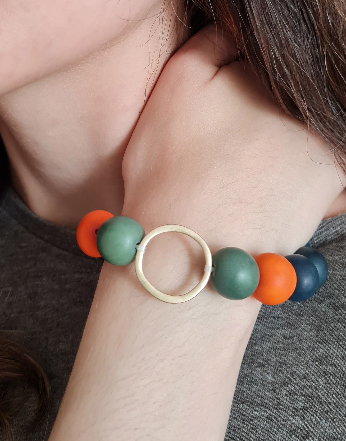 Bola Tagua Bracelet featuring vibrant green and orange colors with a raw brass hoop detail, showcasing its unique design.