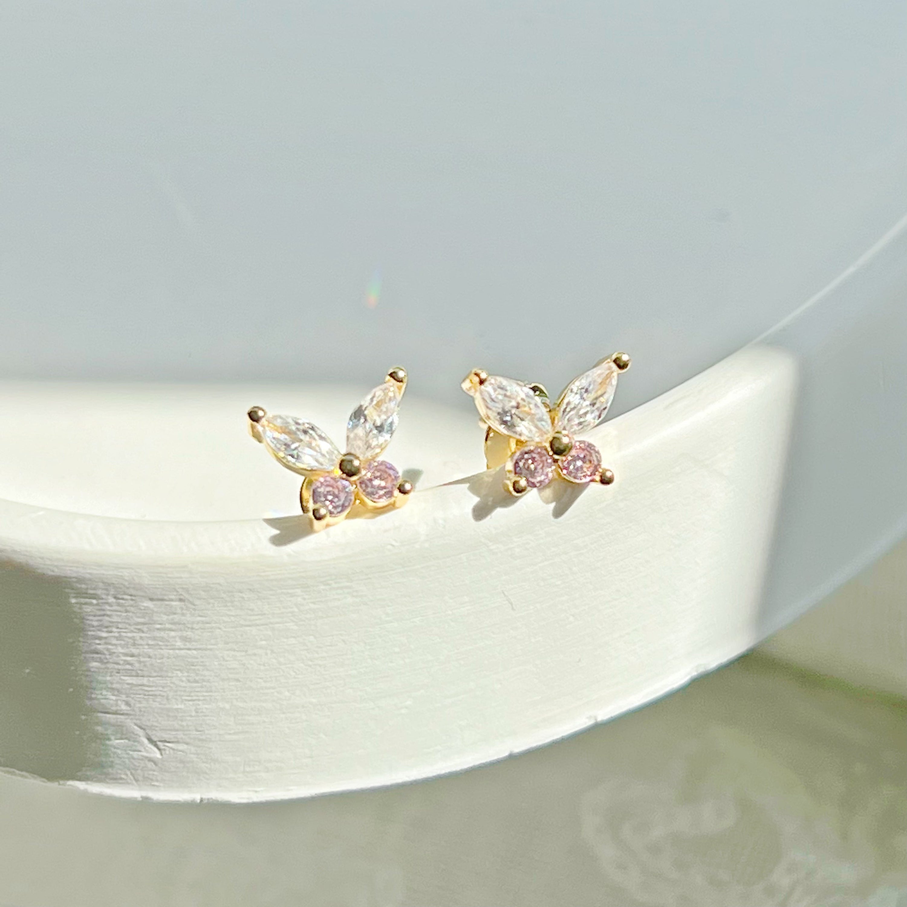 A pair of elegant butterfly gold stud earrings adorned with clear and pink zircon crystals, showcasing their delicate design.
