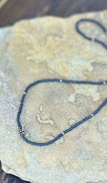 Charcoal grey stretchy seed bead necklace with a metallic gold leaf charm, showcasing elegant design and craftsmanship.