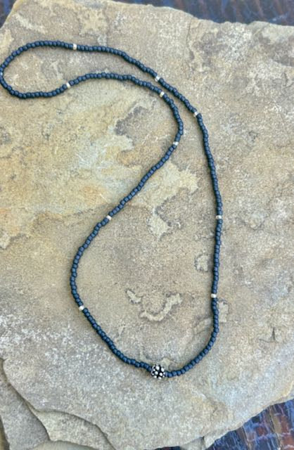 Charcoal grey stretchy seed bead necklace with a metallic gold leaf charm, showcasing elegant design and craftsmanship.