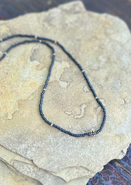 Charcoal grey stretchy seed bead necklace with a metallic gold leaf charm, showcasing elegant design and craftsmanship.