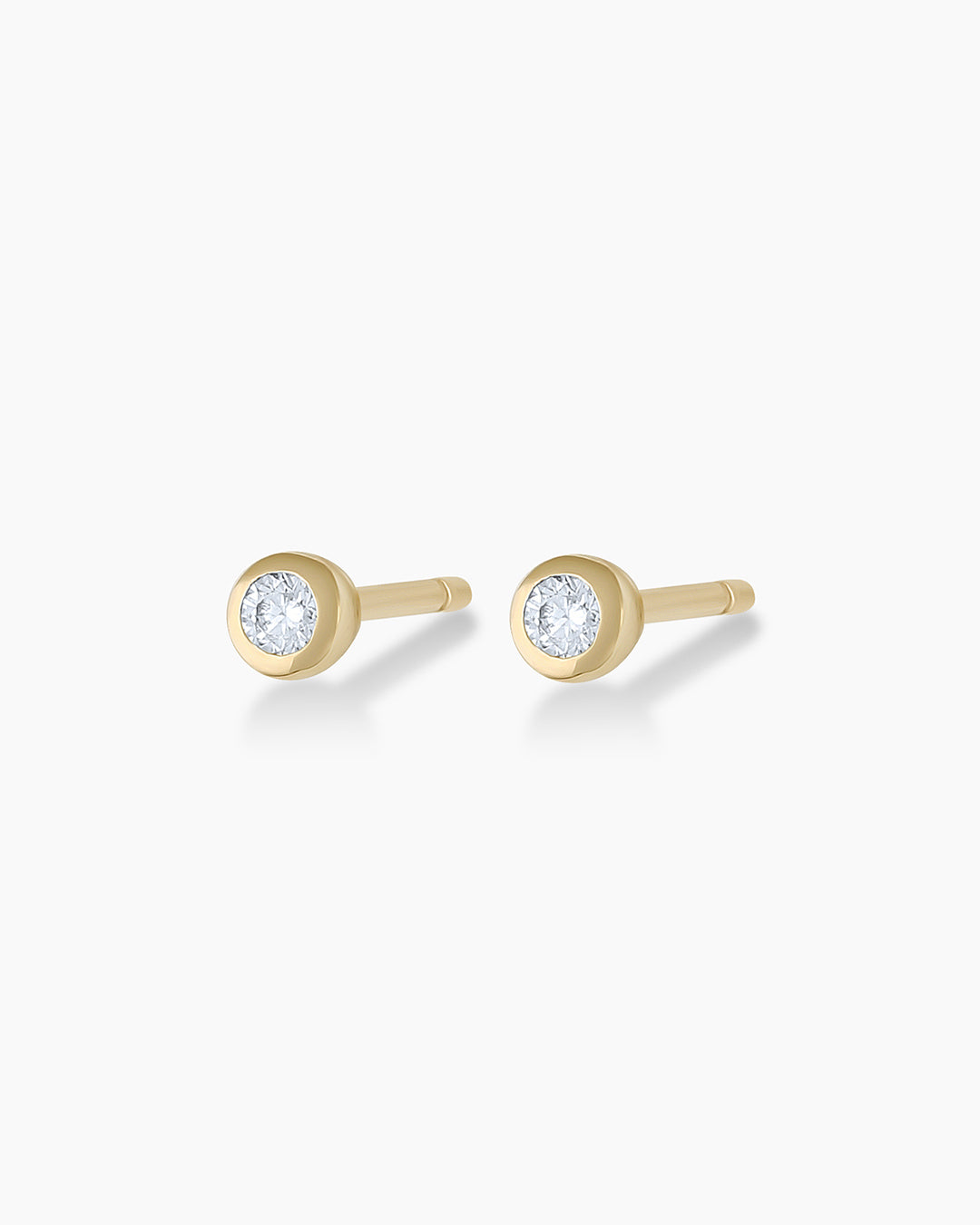 A pair of elegant gold stud earrings featuring round cut, bezel set diamonds, showcasing their brilliance and craftsmanship.