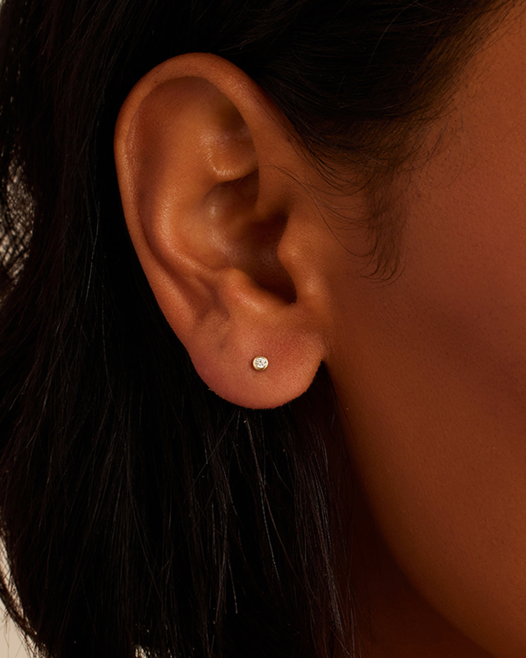 A pair of elegant gold stud earrings featuring round cut, bezel set diamonds, showcasing their brilliance and craftsmanship.