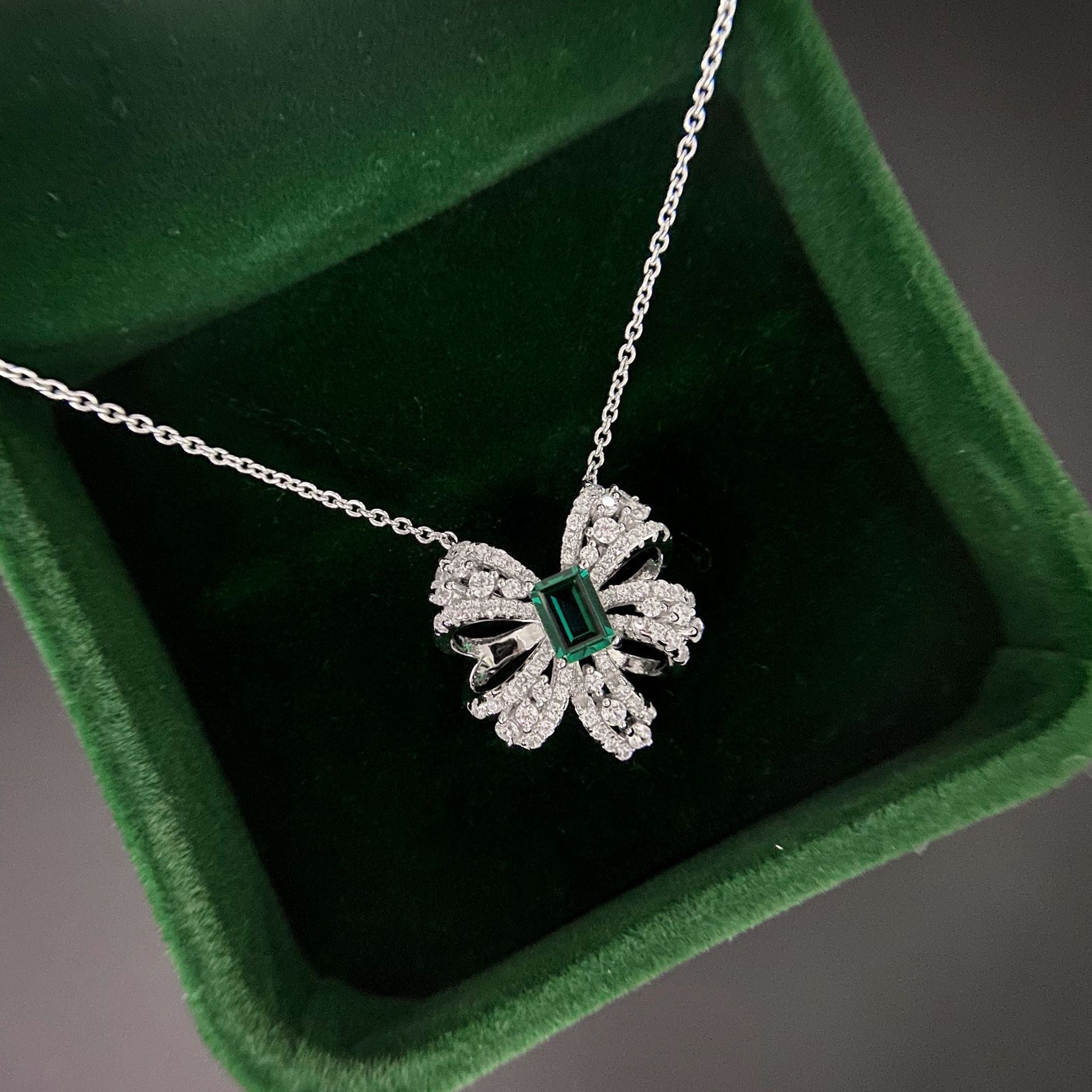 Delicate necklace featuring a created emerald set in 925 sterling silver with white gold finish, adjustable chain.