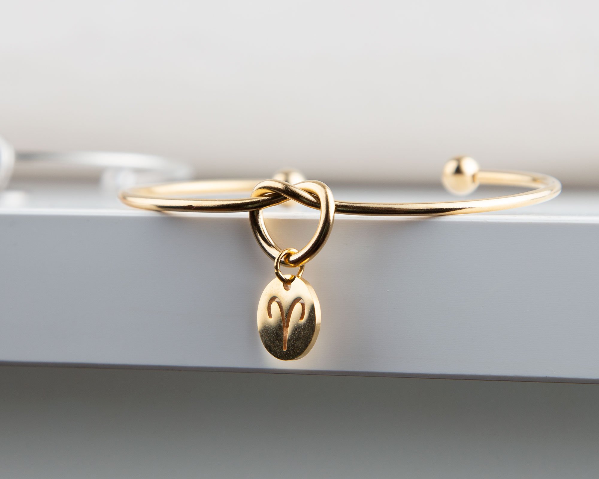 Dainty Knot Bracelet featuring a gold plated wire knot design and a zodiac symbol charm, elegantly displayed on a soft background.