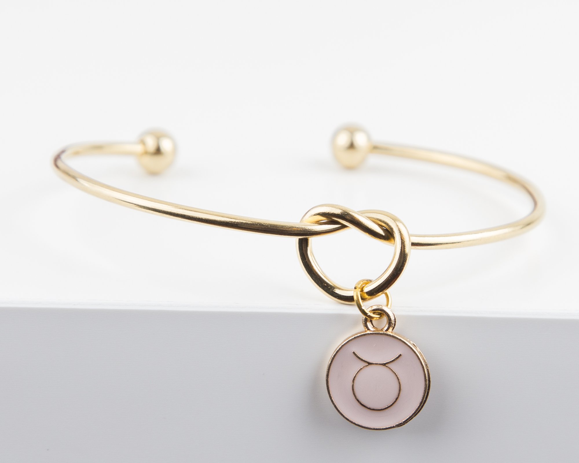 Dainty Knot Bracelet featuring a gold plated wire knot design and a zodiac symbol charm, elegantly displayed on a soft background.