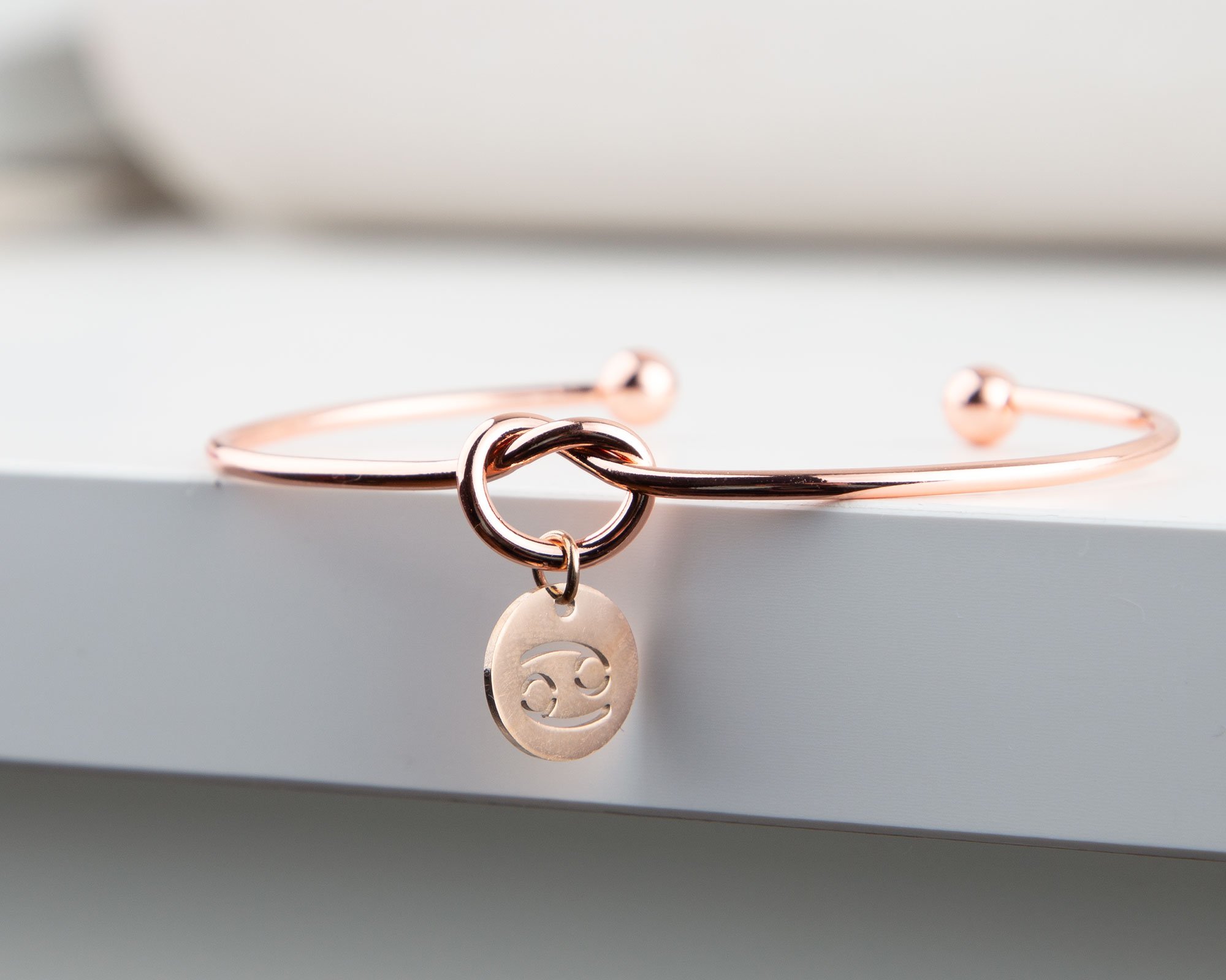 Dainty Knot Bracelet featuring a rose gold plated wire knot design with a zodiac charm, elegantly displayed on a soft background.