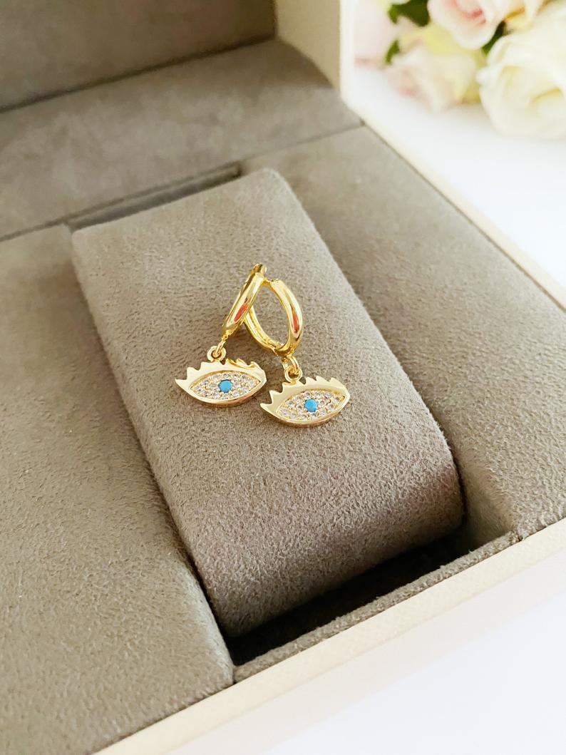 A pair of handmade gold dangle evil eye earrings featuring a delicate design, perfect for adding elegance and protection to any outfit.