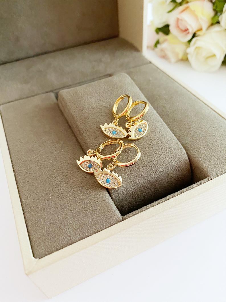 A pair of handmade gold dangle evil eye earrings featuring a delicate design, perfect for adding elegance and protection to any outfit.