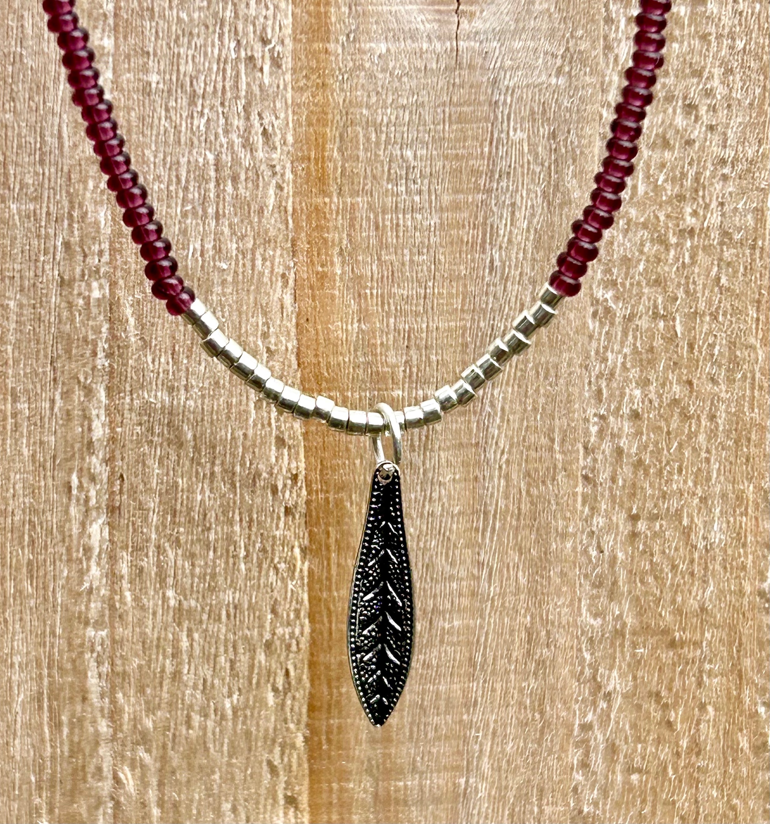 Dark purple boho seed bead necklace featuring a silver feather pendant, showcasing vibrant Czech seed beads and a stylish design.