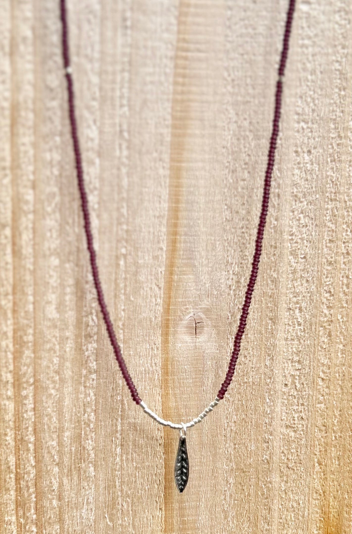 Dark purple boho seed bead necklace featuring a silver feather pendant, showcasing vibrant Czech seed beads and a stylish design.