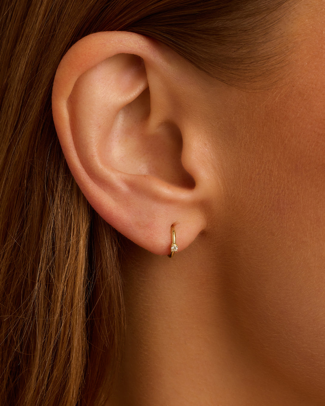 A pair of elegant Diamond Solitaire Huggies featuring a glimmering diamond solitaire, showcasing their timeless and versatile design.