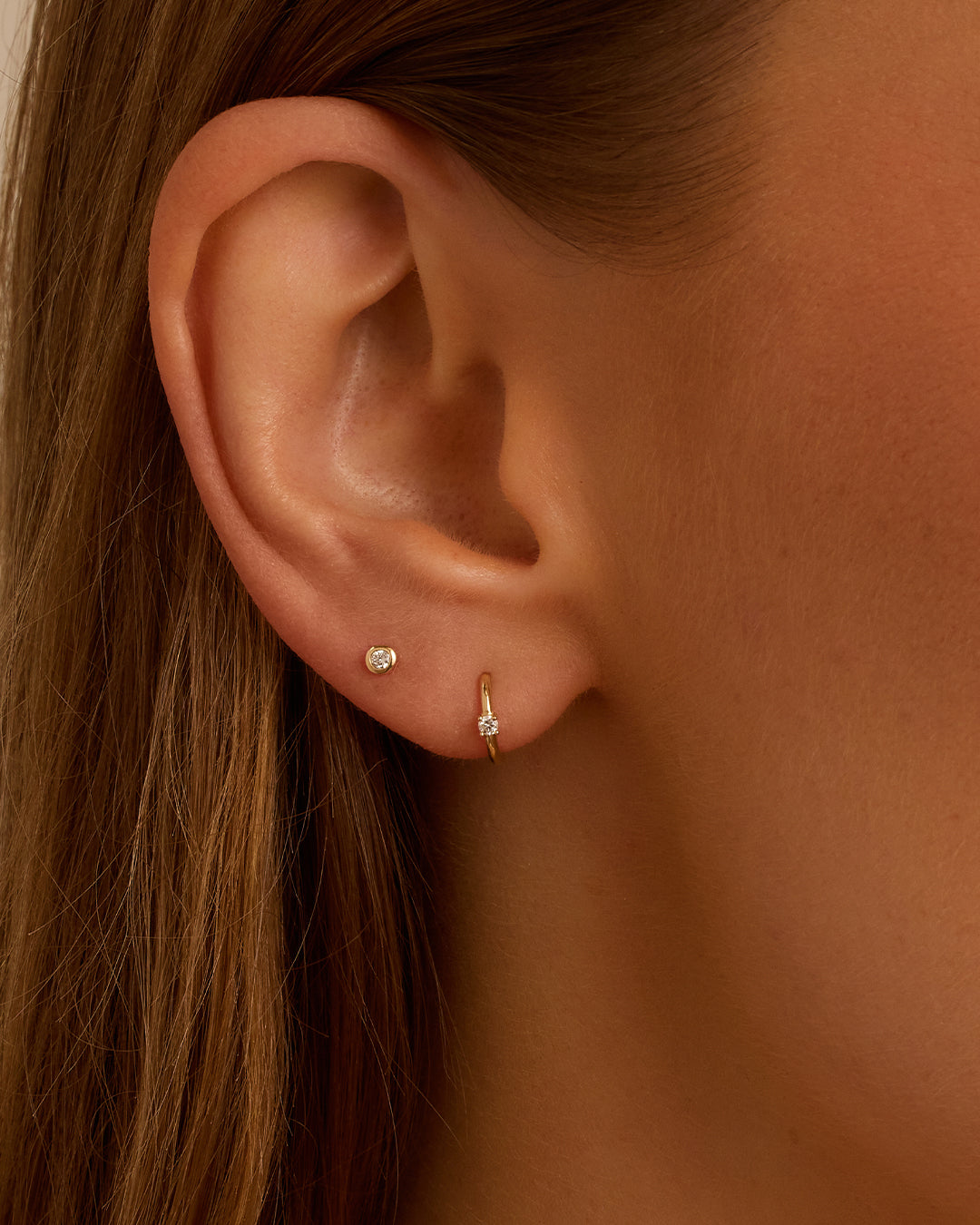 A pair of elegant Diamond Solitaire Huggies featuring a glimmering diamond solitaire, showcasing their timeless and versatile design.