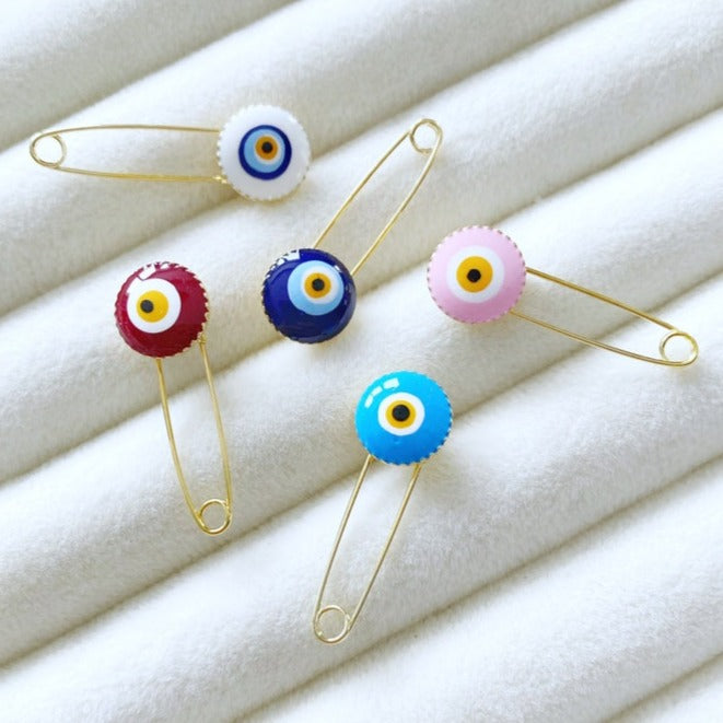 Evil Eye Baby Pin featuring a brass safety pin with an evil eye charm, designed for newborn protection and special occasions.