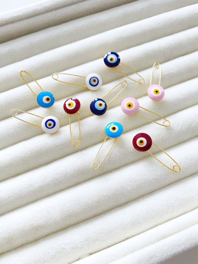 Evil Eye Baby Pin featuring a brass safety pin with an evil eye charm, designed for newborn protection and special occasions.