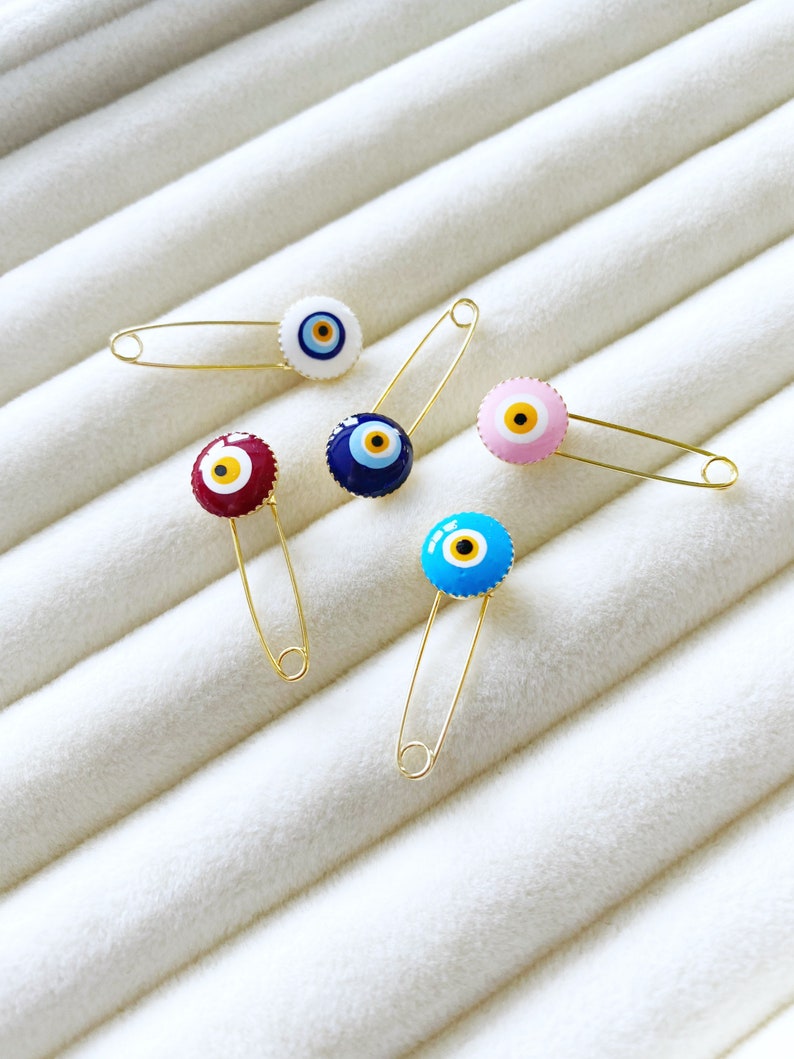 Evil Eye Baby Pin featuring a brass safety pin with an evil eye charm, designed for newborn protection and special occasions.