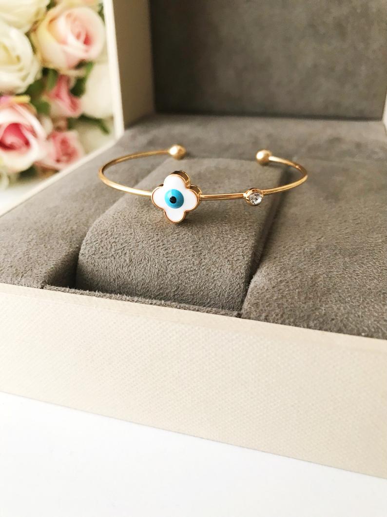 Evil Eye Bangle Bracelet featuring a movable oval charm and clover design in various colors, made from durable stainless steel.
