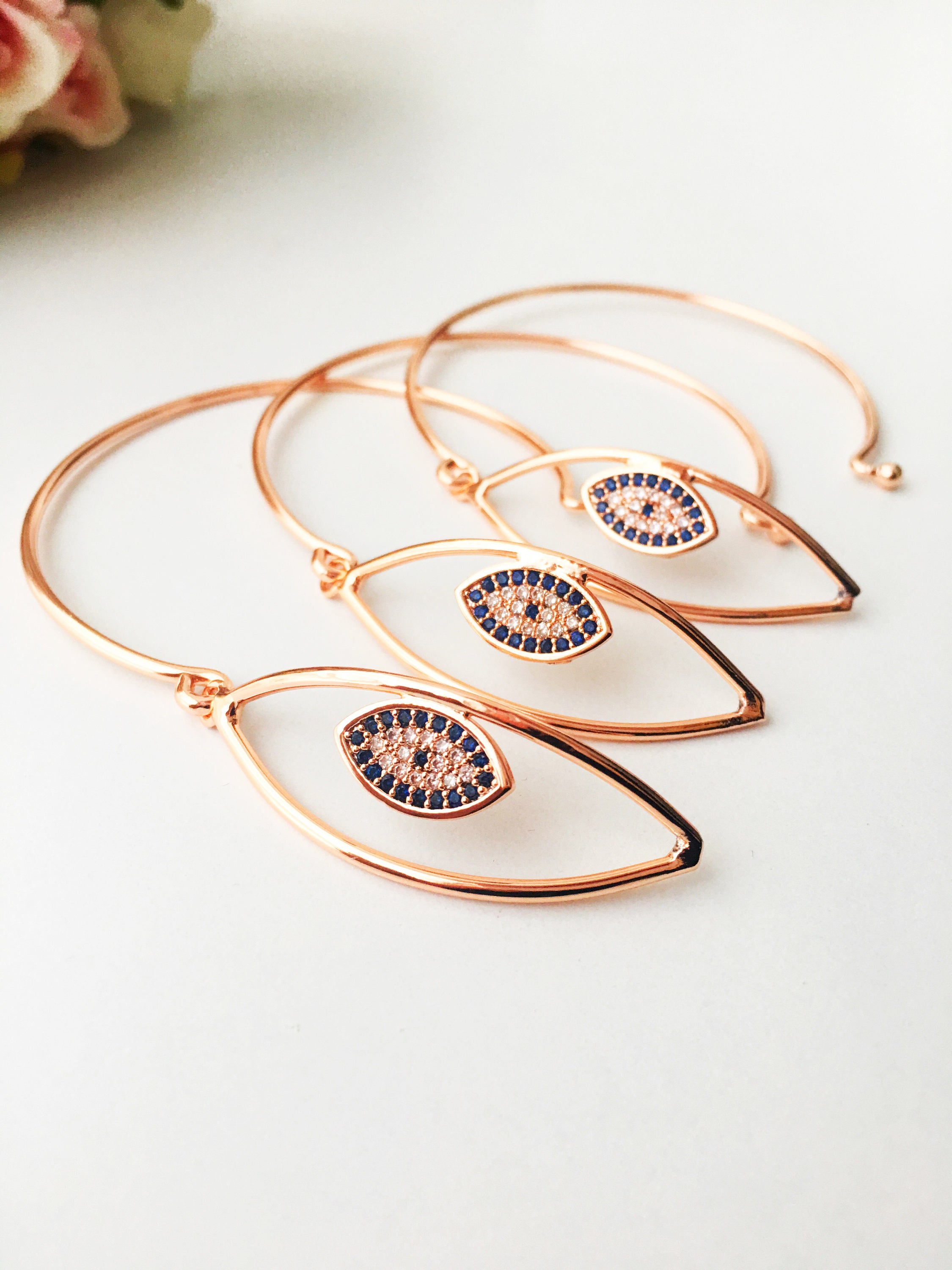 A beautiful rose gold Evil Eye Bangle Bracelet featuring a movable oval charm and zircon accents, showcasing its elegant design.