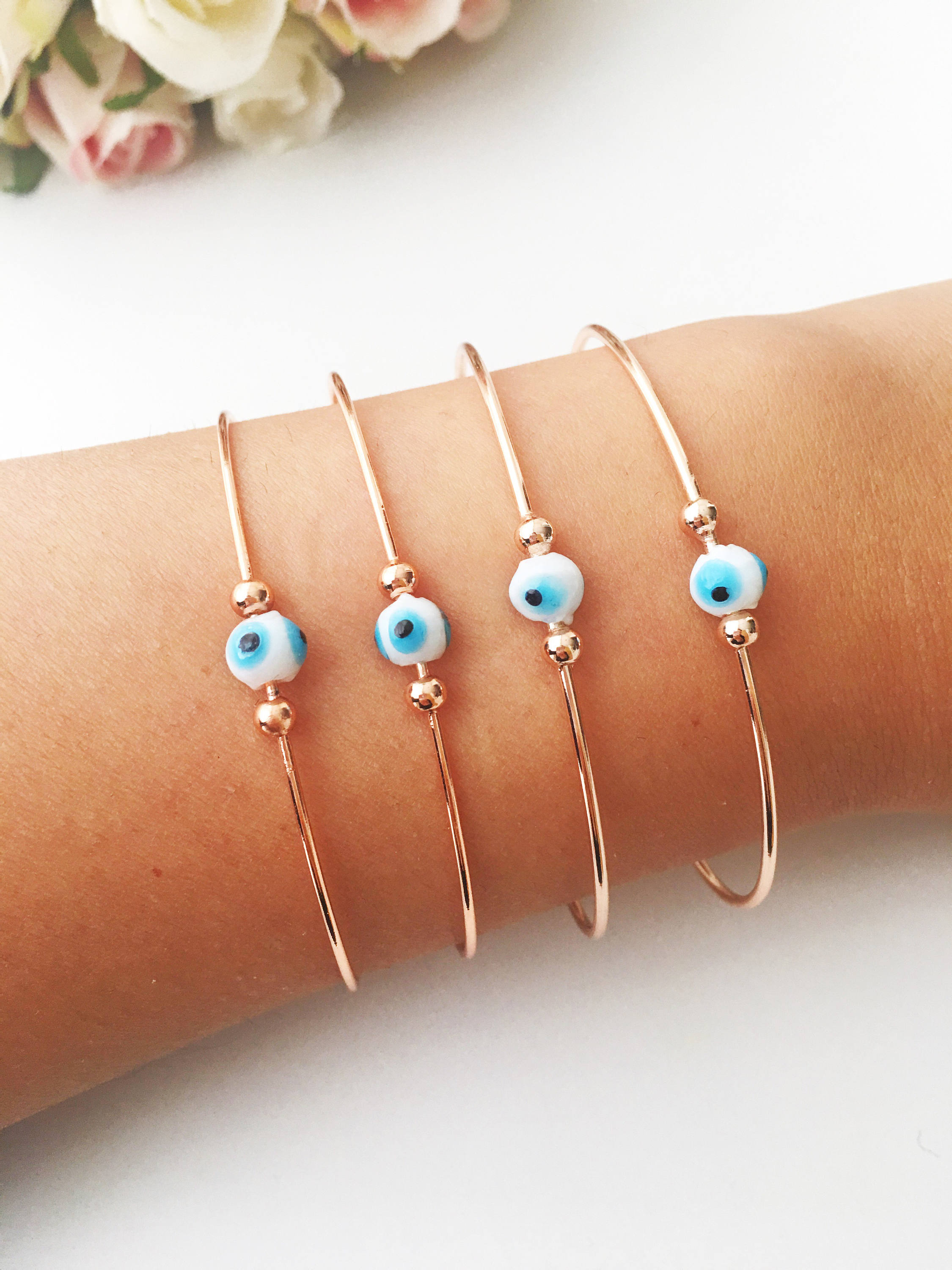 Evil Eye Beaded Bangle Bracelet in Gold Rose featuring a movable blue evil eye charm and adjustable stainless steel design.