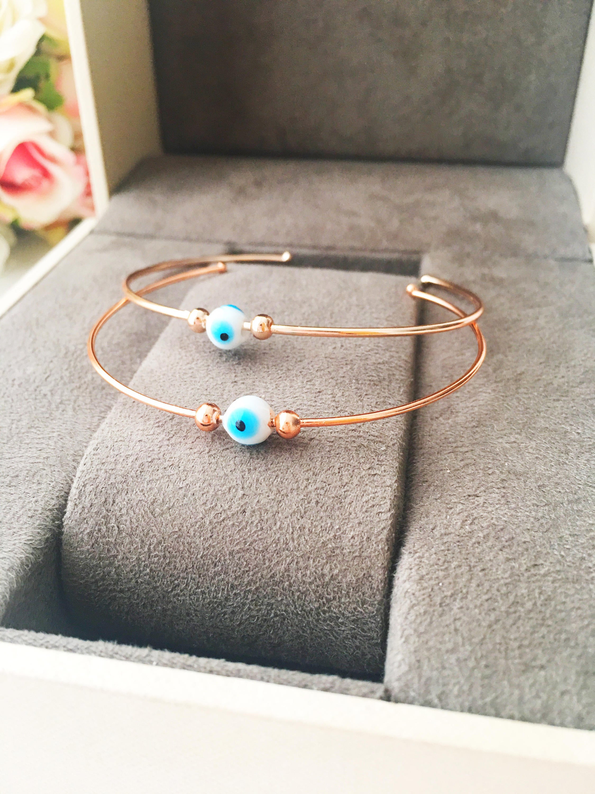 Evil Eye Beaded Bangle Bracelet in Gold Rose featuring a movable blue evil eye charm and adjustable stainless steel design.