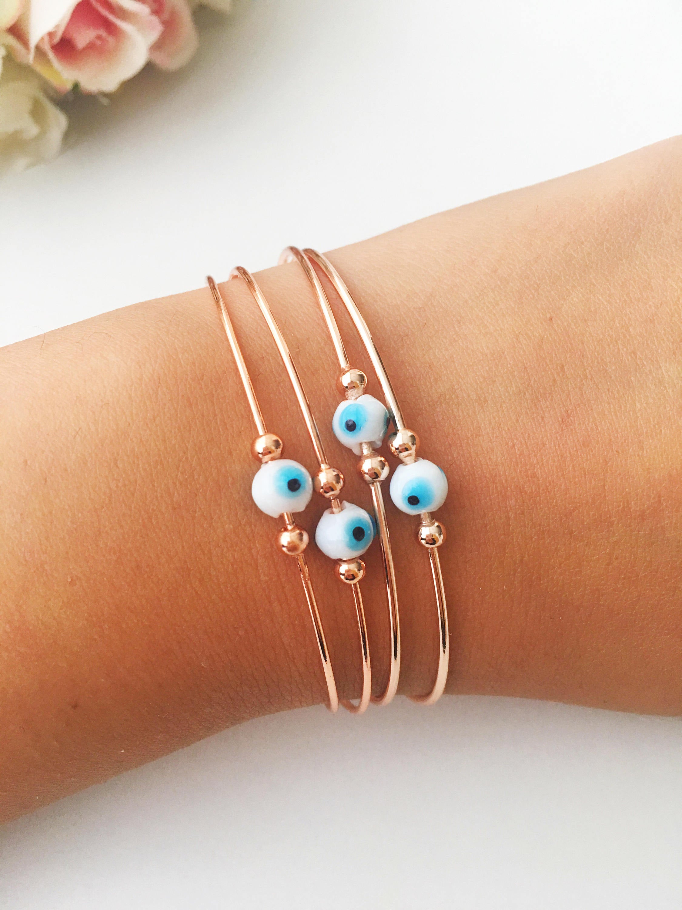 Evil Eye Beaded Bangle Bracelet in Gold Rose featuring a movable blue evil eye charm and adjustable stainless steel design.