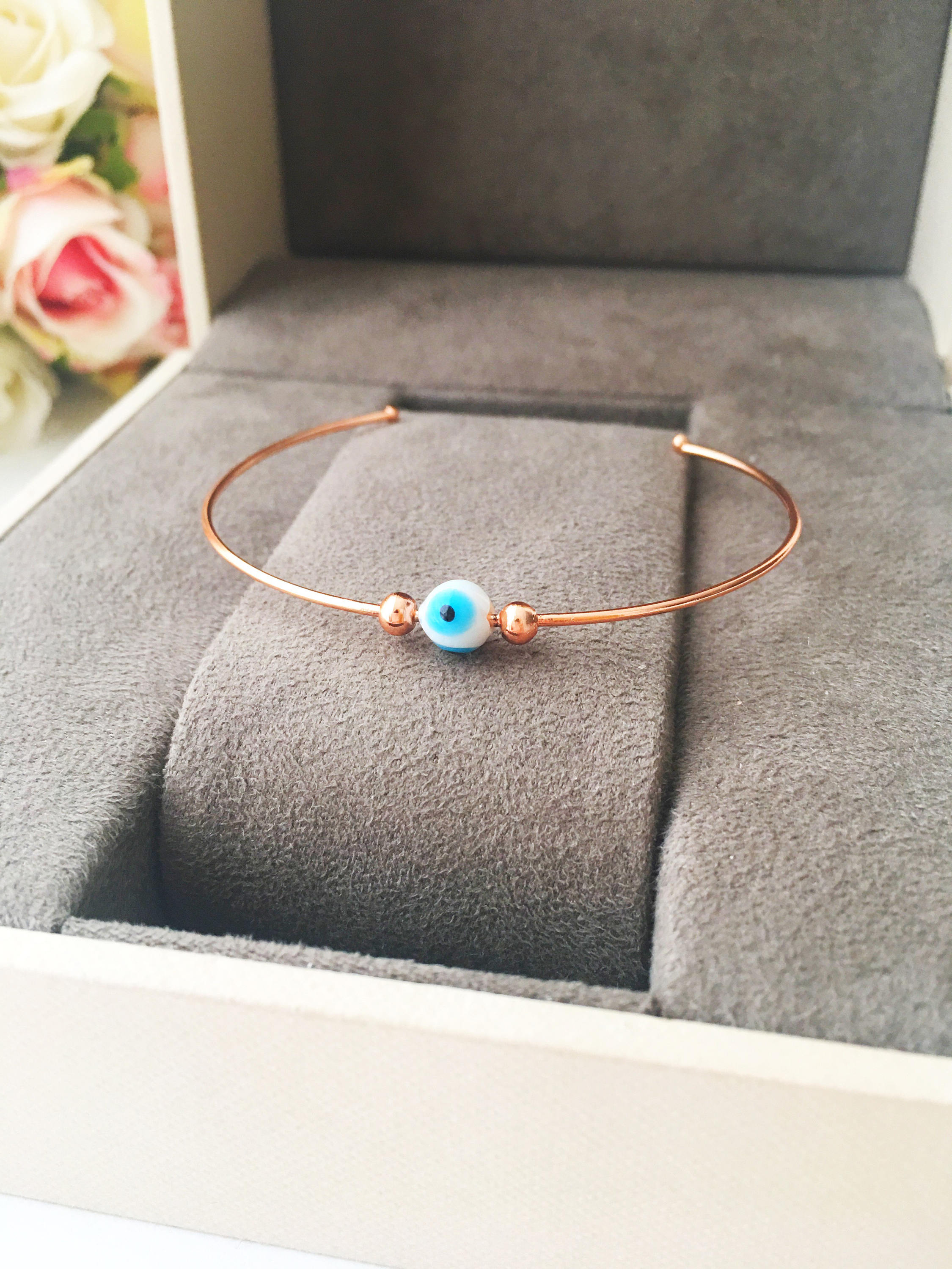 Evil Eye Beaded Bangle Bracelet in Gold Rose featuring a movable blue evil eye charm and adjustable stainless steel design.