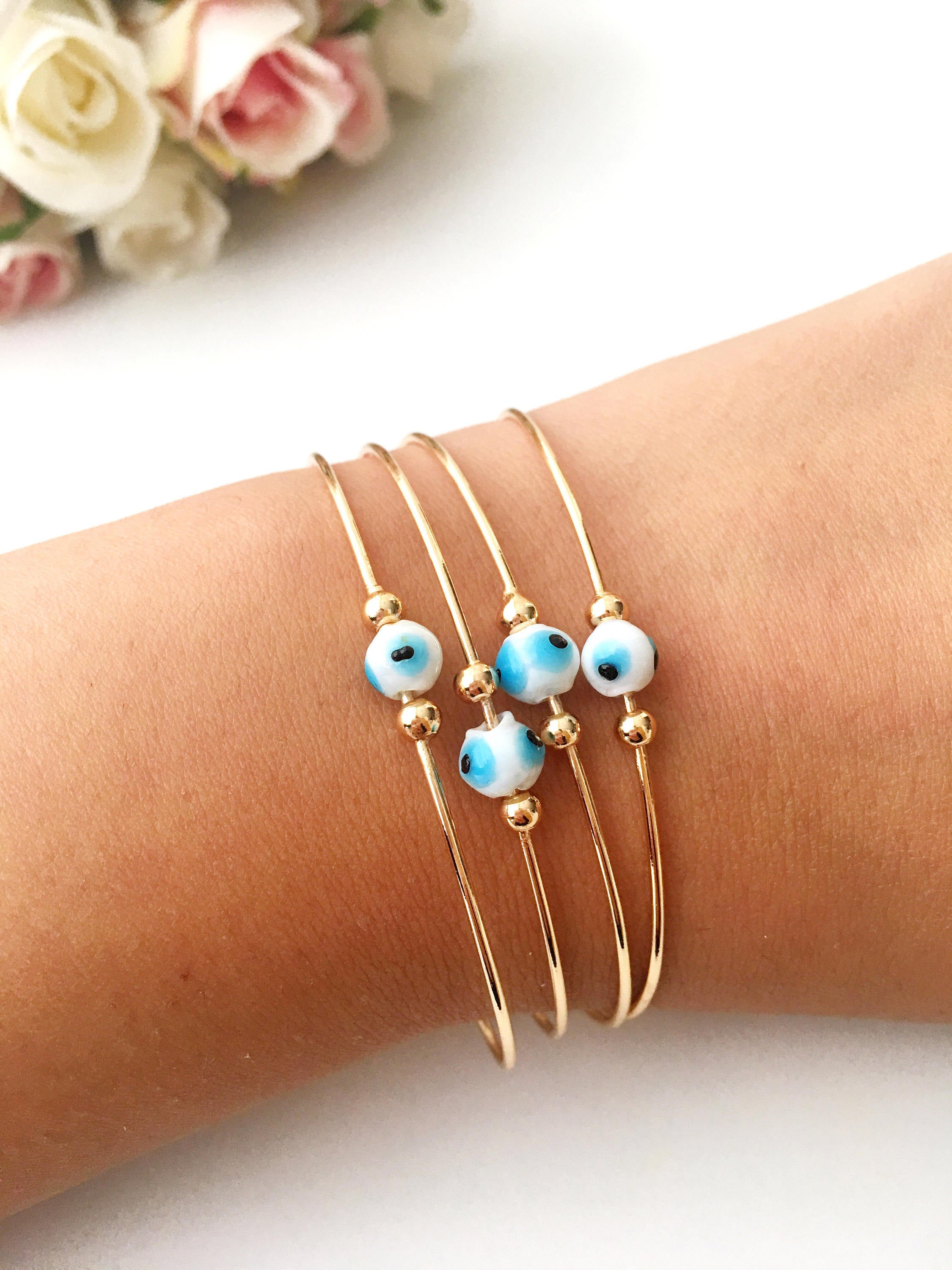 Evil Eye Beaded Bangle Bracelet in Gold Rose featuring a movable blue evil eye charm and adjustable stainless steel design.