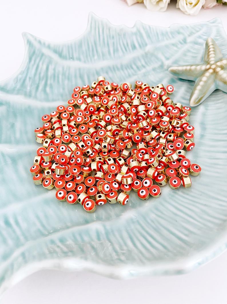 A collection of vibrant orange evil eye beads made of brass, featuring gold connectors, ideal for DIY jewelry making.