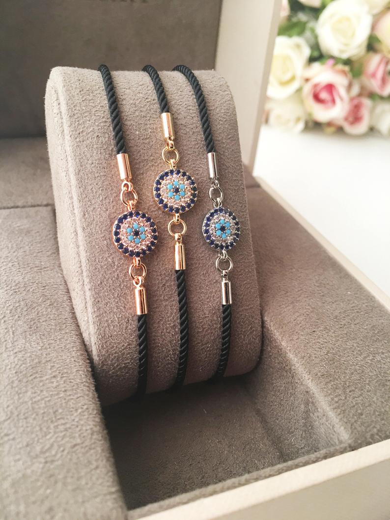 Adjustable Evil Eye Bracelet featuring a black string and a protective charm, available in silver, gold, and rose gold.