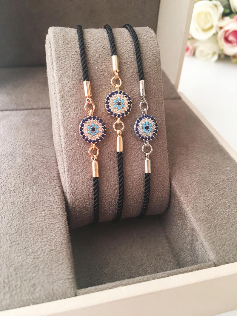 Adjustable Evil Eye Bracelet featuring a black string and a protective charm, available in silver, gold, and rose gold.
