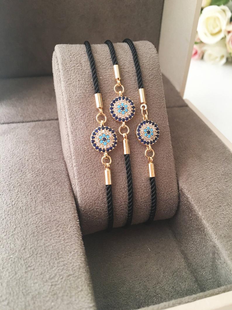 Adjustable Evil Eye Bracelet featuring a black string and a protective charm, available in silver, gold, and rose gold.