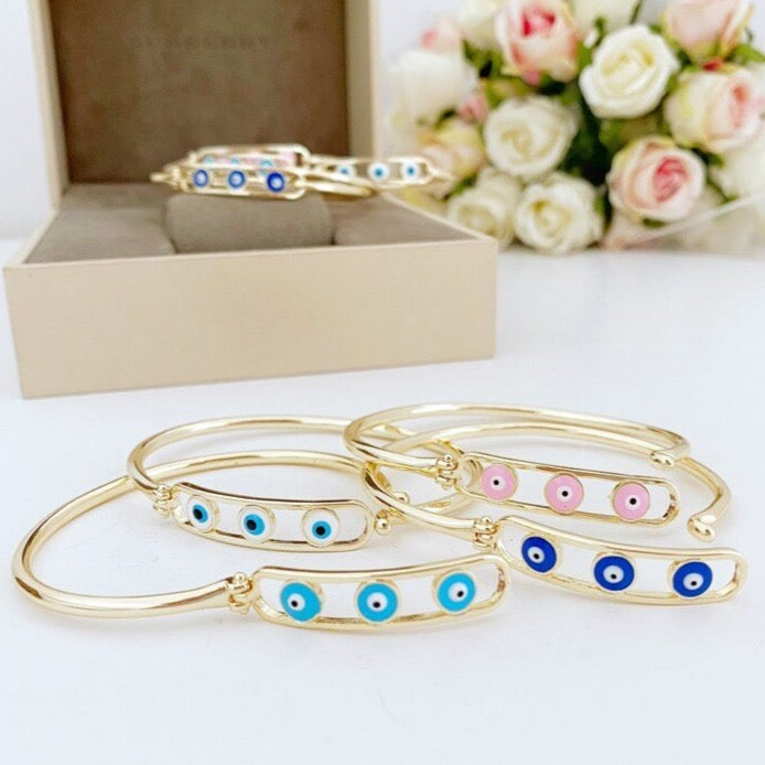 Elegant gold bangle bracelet featuring a movable evil eye charm, available in blue, white, pink, and turquoise colors.