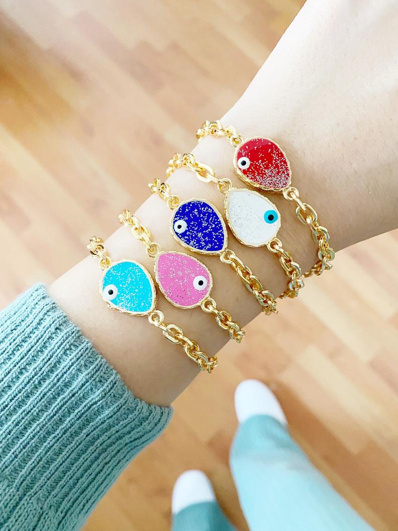 A beautiful Evil Eye Bracelet featuring a gold chain and a glittering teardrop evil eye charm, available in multiple colors.