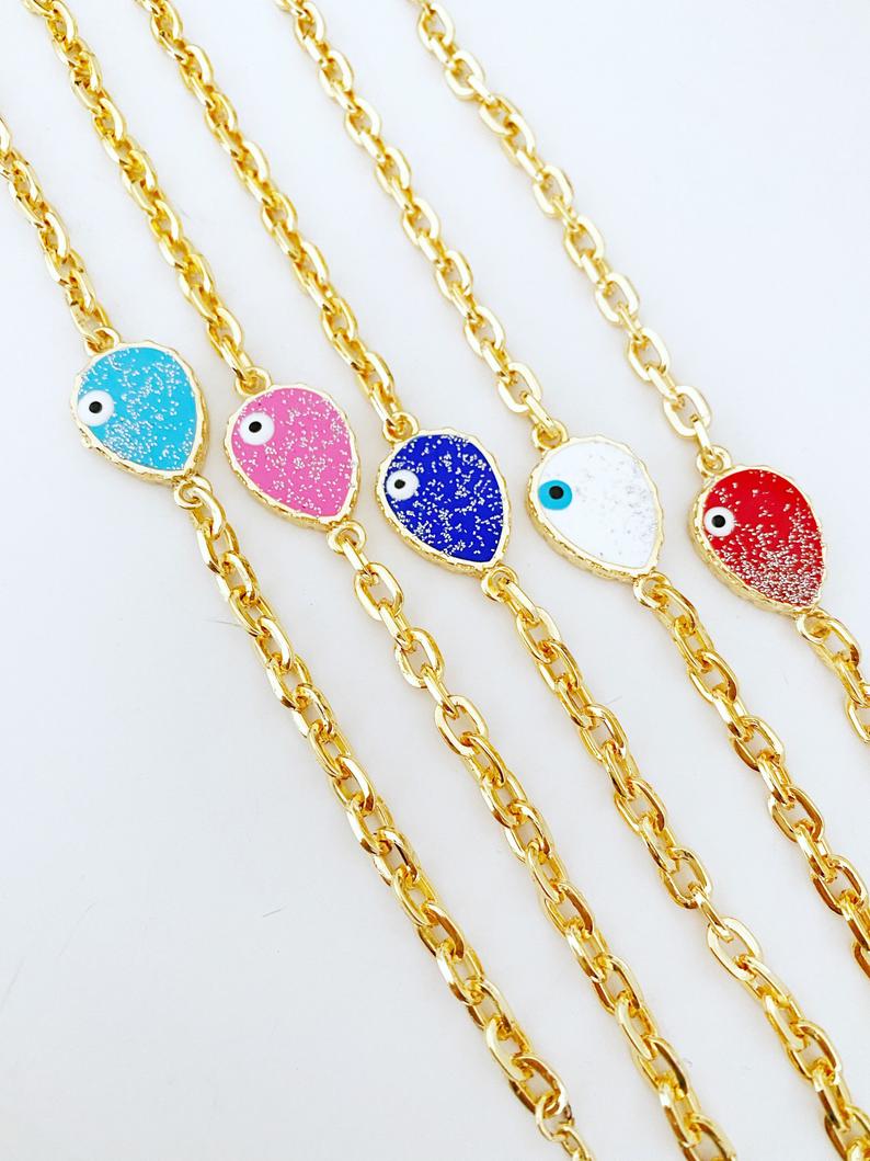 A beautiful Evil Eye Bracelet featuring a gold chain and a glittering teardrop evil eye charm, available in multiple colors.