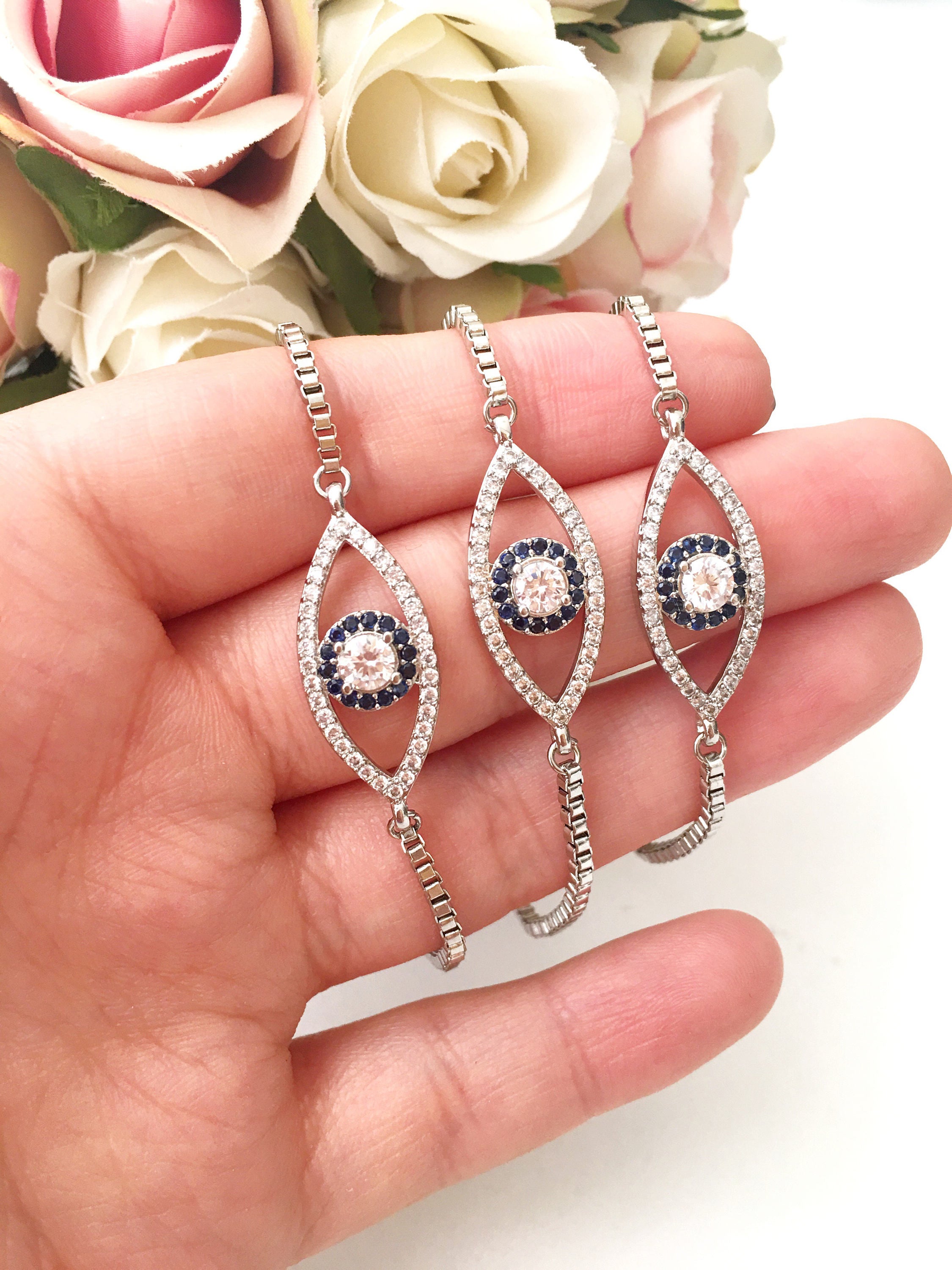 A collection of handmade silver evil eye bracelets featuring various designs including safety pin, beaded, and zirconia styles.