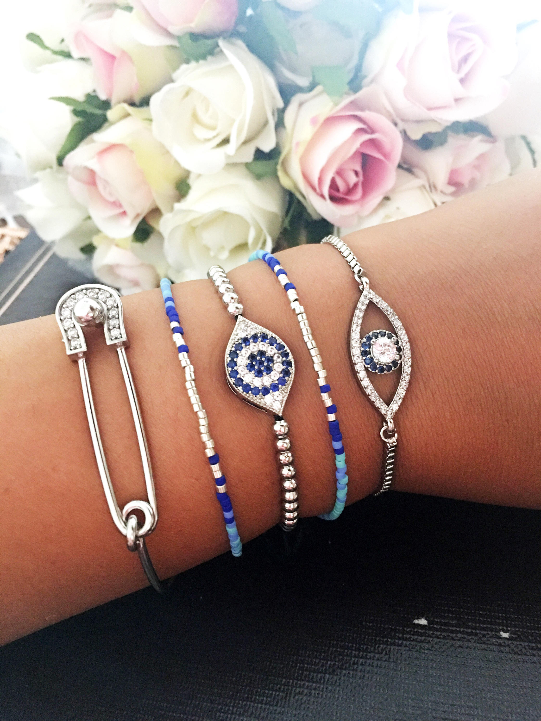 A collection of handmade silver evil eye bracelets featuring various designs including safety pin, beaded, and zirconia styles.