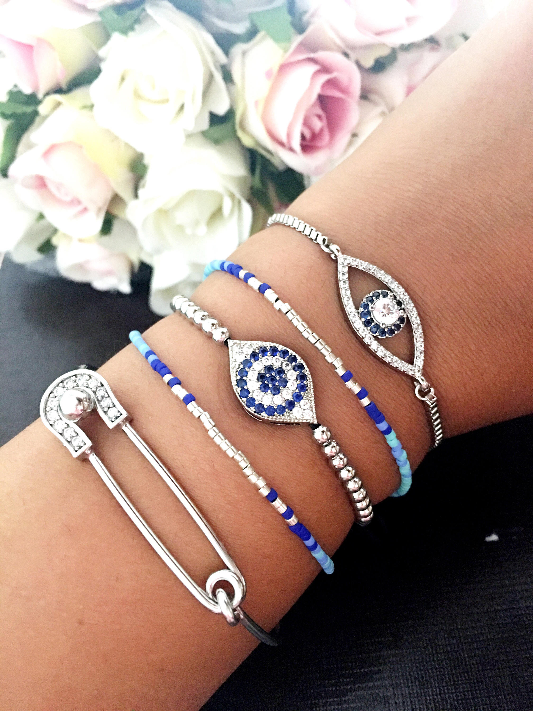 A collection of handmade silver evil eye bracelets featuring various designs including safety pin, beaded, and zirconia styles.
