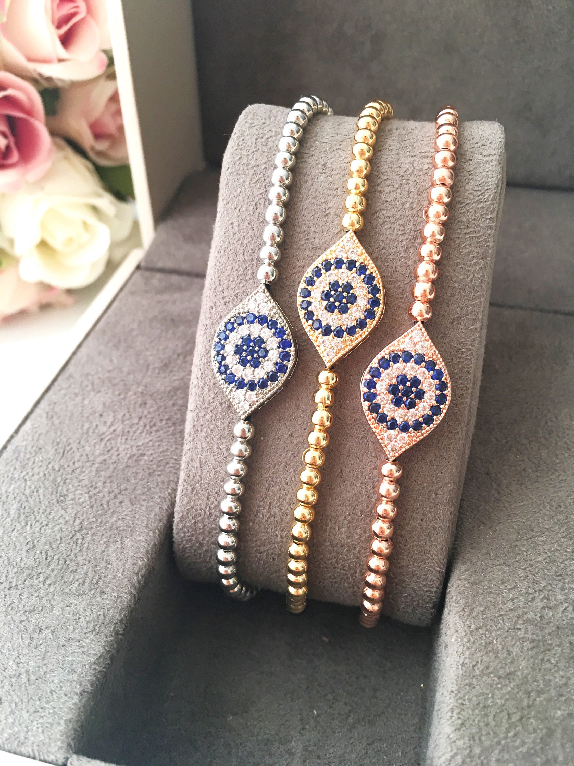 A collection of handmade silver evil eye bracelets featuring various designs including safety pin, beaded, and zirconia styles.