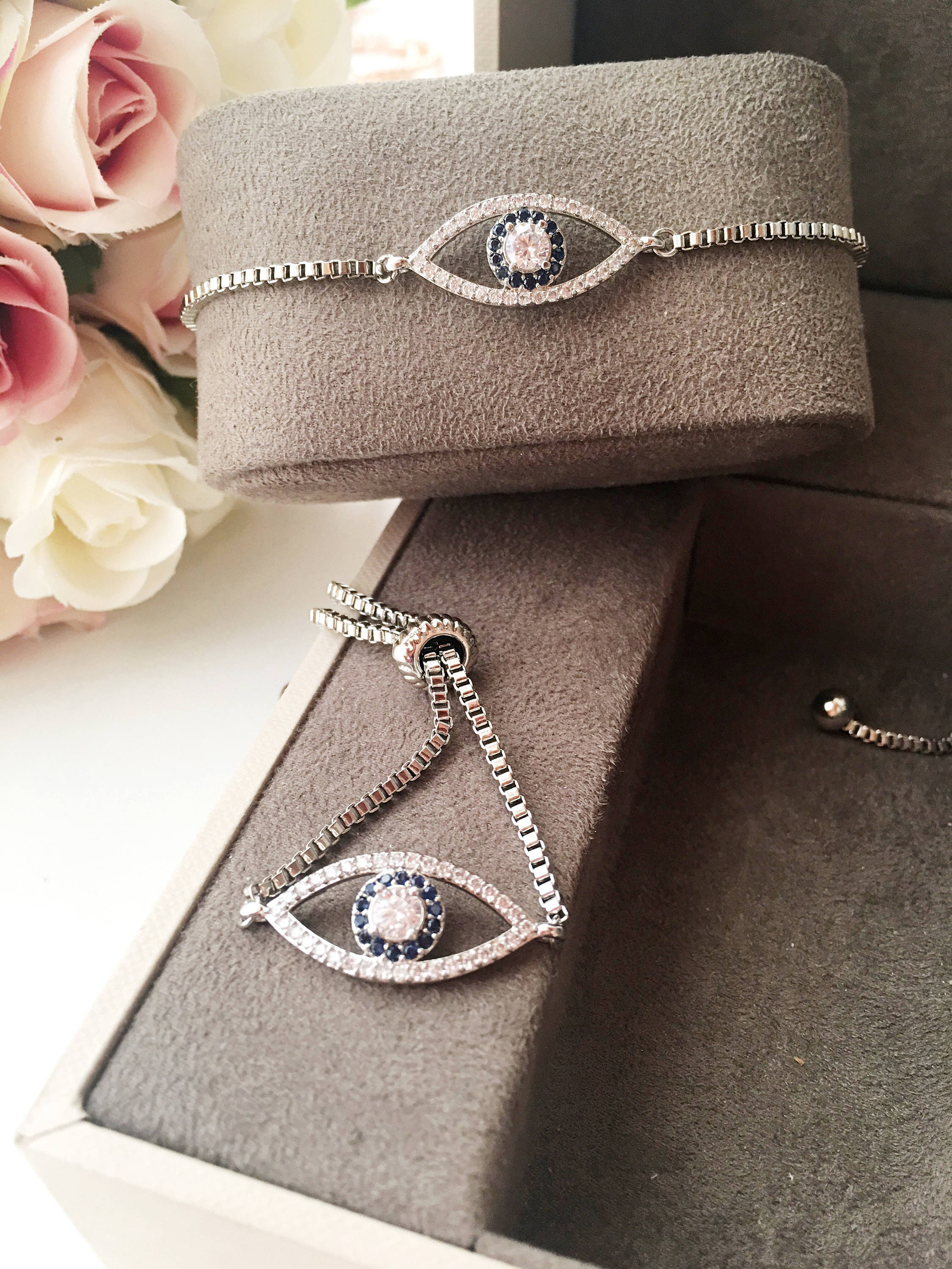 A collection of handmade silver evil eye bracelets featuring various designs including safety pin, beaded, and zirconia styles.