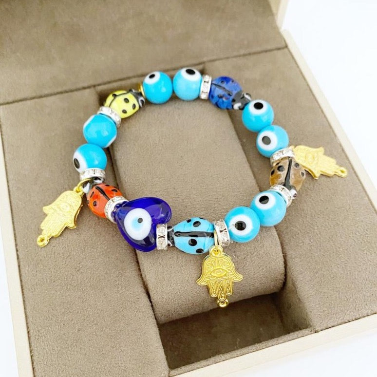 Evil Eye Bracelet featuring turquoise beads, gold hamsa charm, and ladybug charm, showcasing a stylish and protective design.